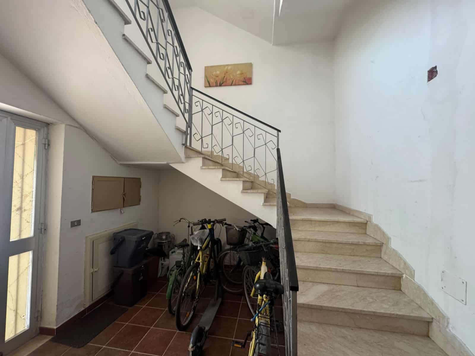 Ingresso di un appartamento con biciclette parcheggiate sotto le scale in un ambiente luminoso e semplice.