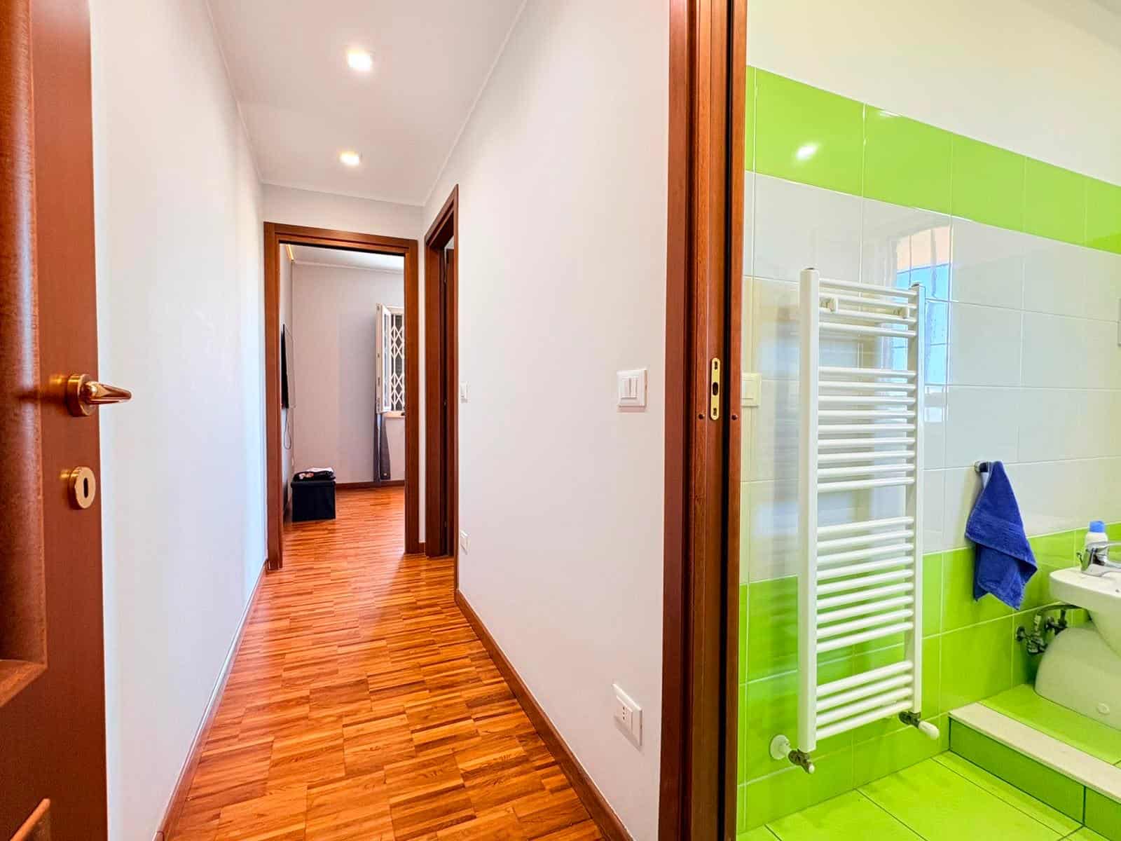 Interno di un appartamento in vendita a Milazzo, vista corridoio con pavimento in legno e pareti bianche.