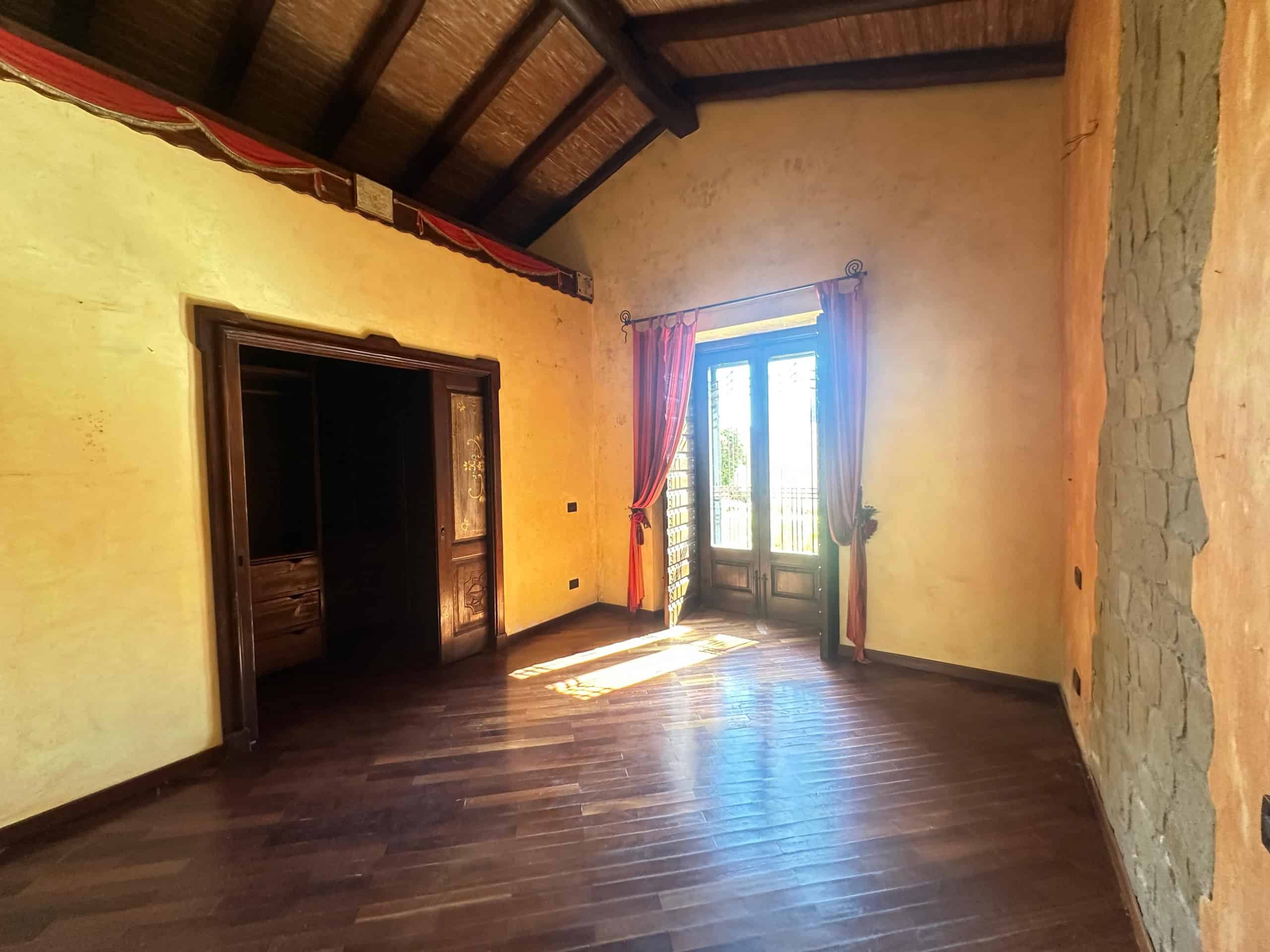 Interno di una villa in vendita a Milazzo con pareti gialle, pavimento in legno e grandi porte con tende colorate.