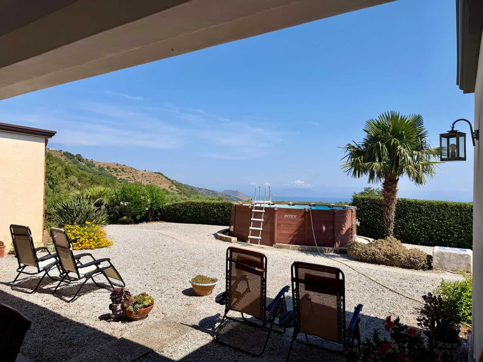 Vista panoramica di un giardino con piscina, sedie a sdraio e vista sul mare e le colline circostanti.