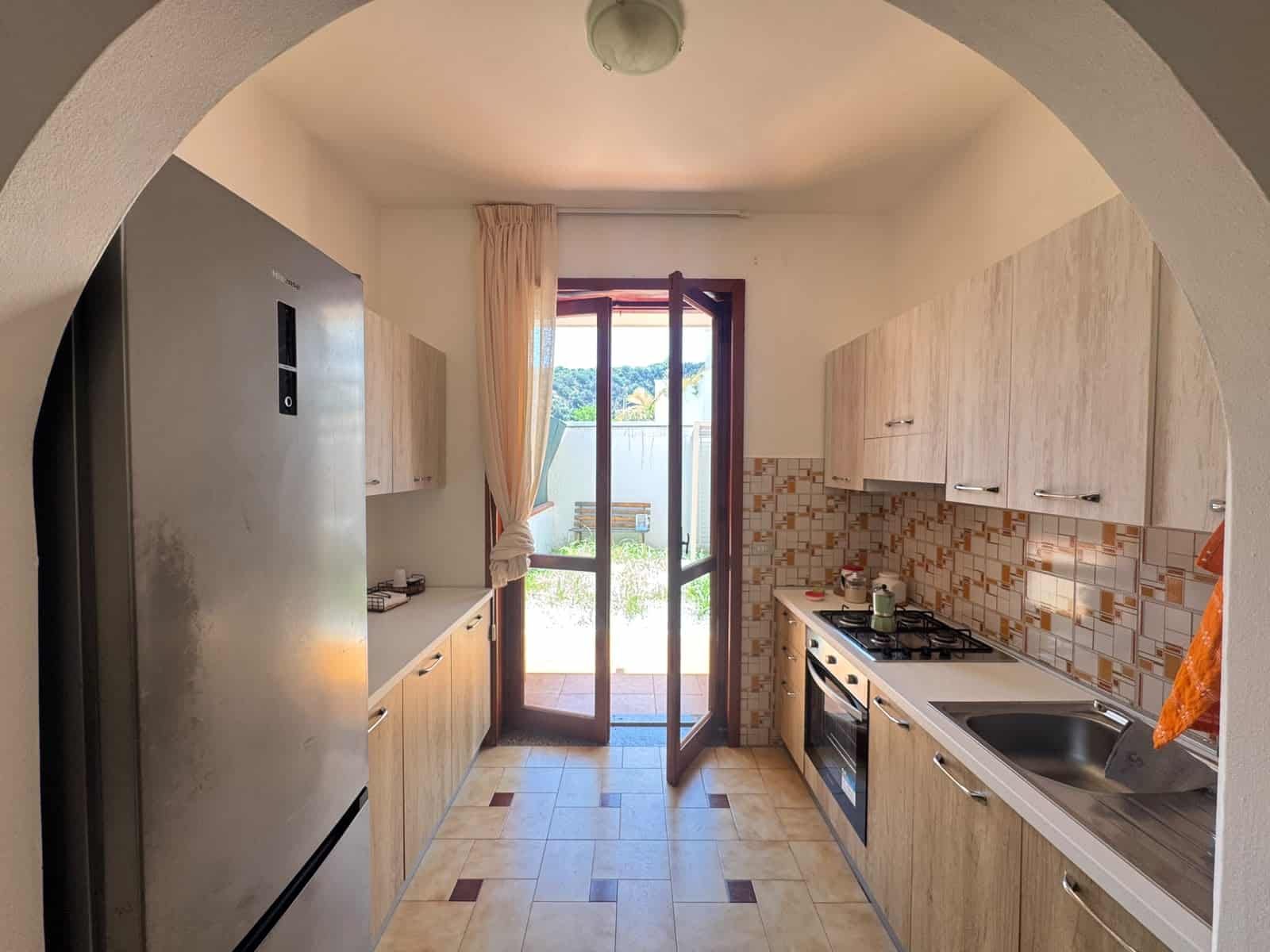 Cucina moderna in villa in vendita a Milazzo, con mobili in legno chiaro, forno, piano cottura e accesso al giardino esterno.