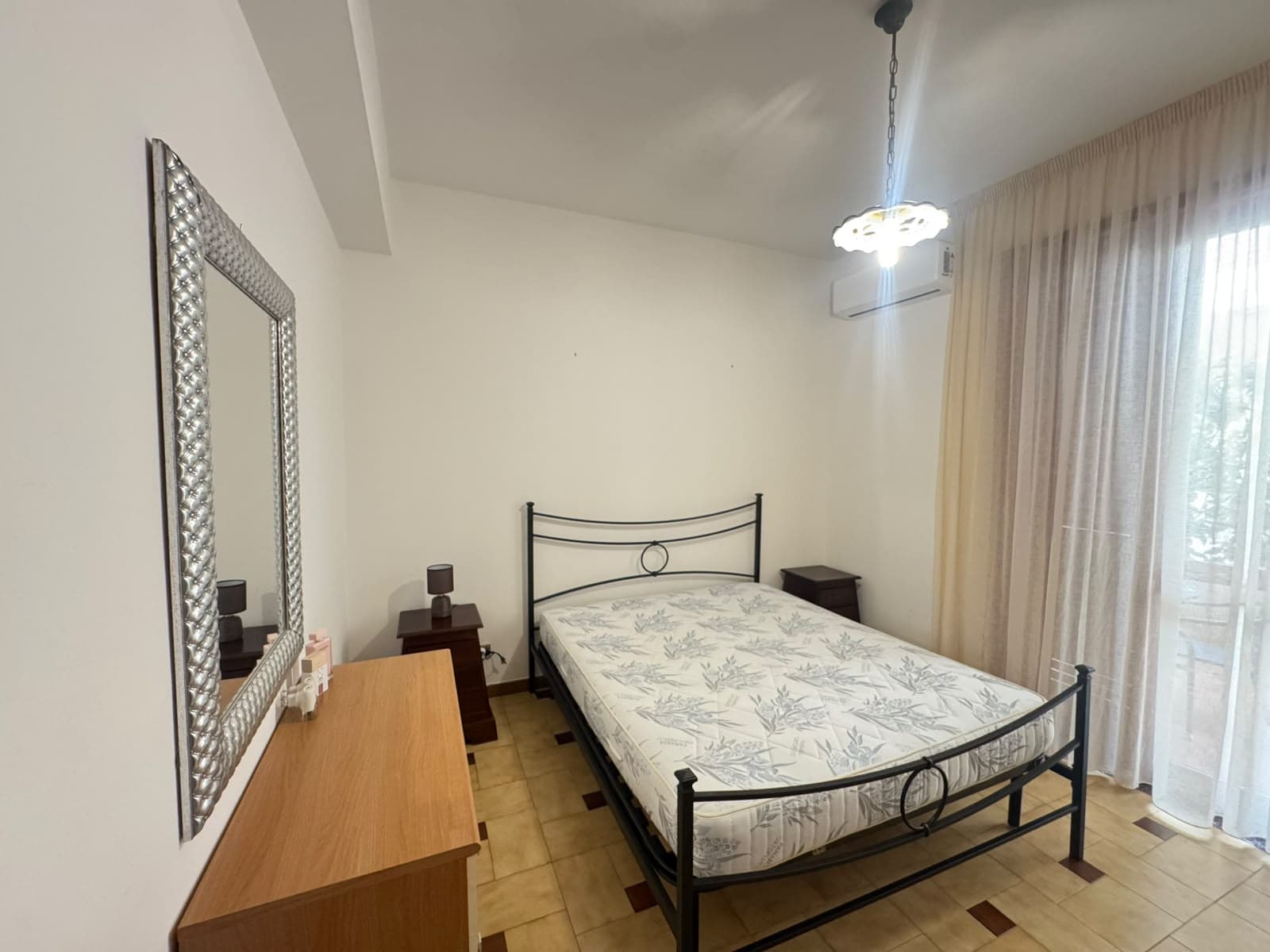 Camera da letto con letto matrimoniale, armadio e grande finestra con tende leggere, ambiente luminoso e accogliente.