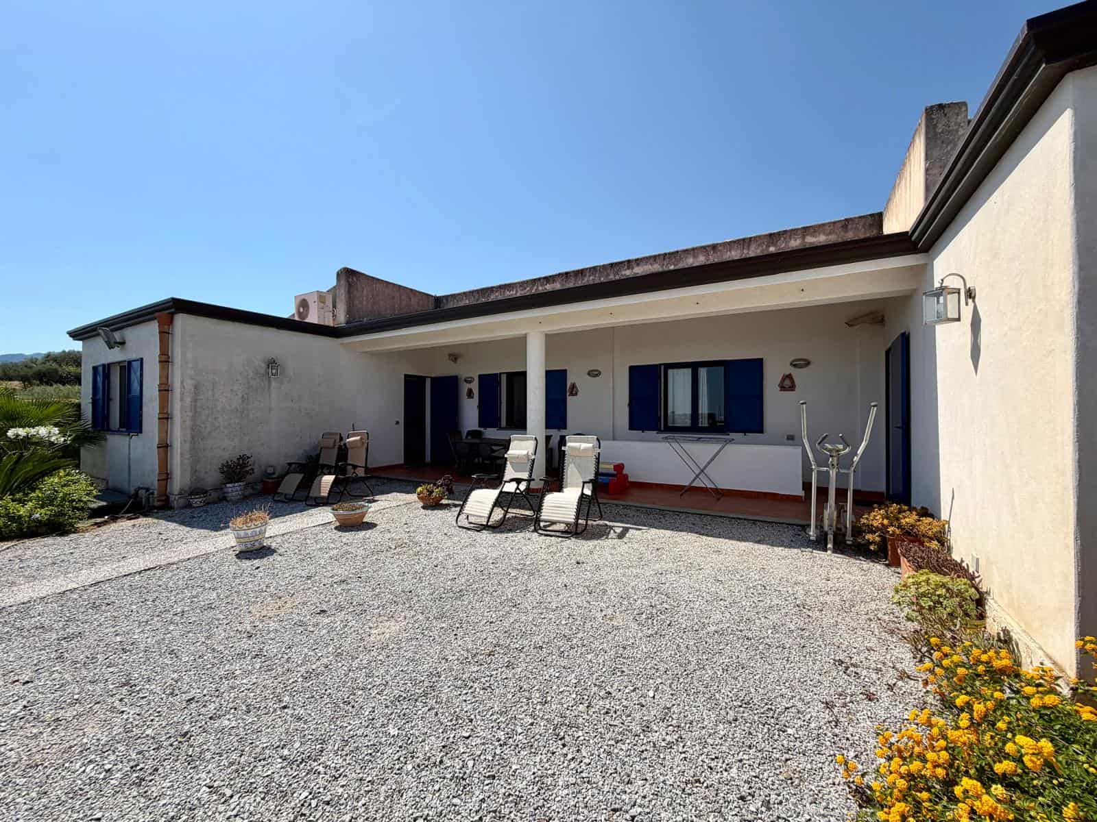 Esterno di una casa moderna con patio e sedie a sdraio, sotto un cielo sereno, in un ambiente tranquillo e ben curato.