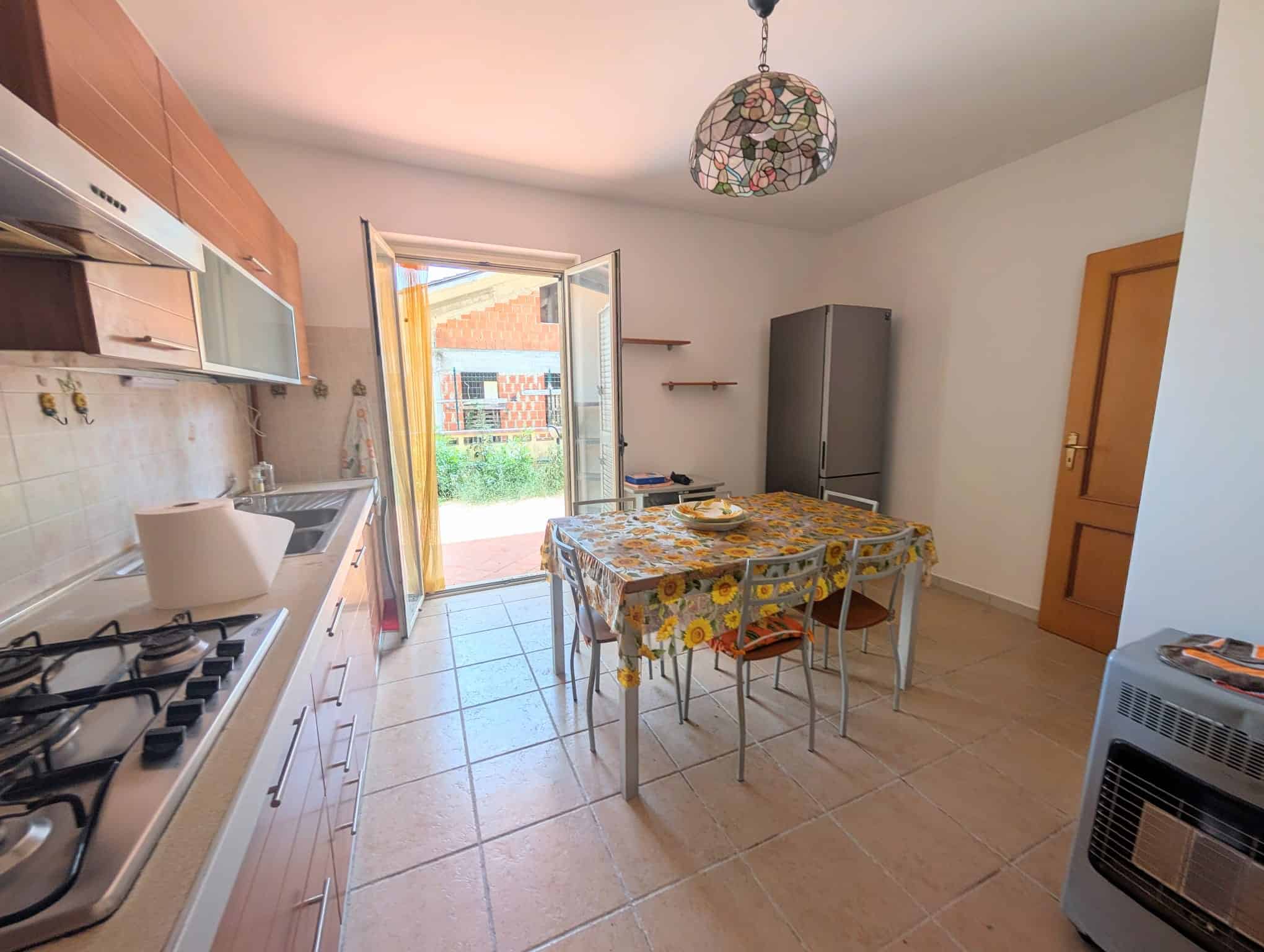 Cucina luminosa con porta finestra che dà su un giardino, tavolo da pranzo con tovaglia floreale e mobili moderni.