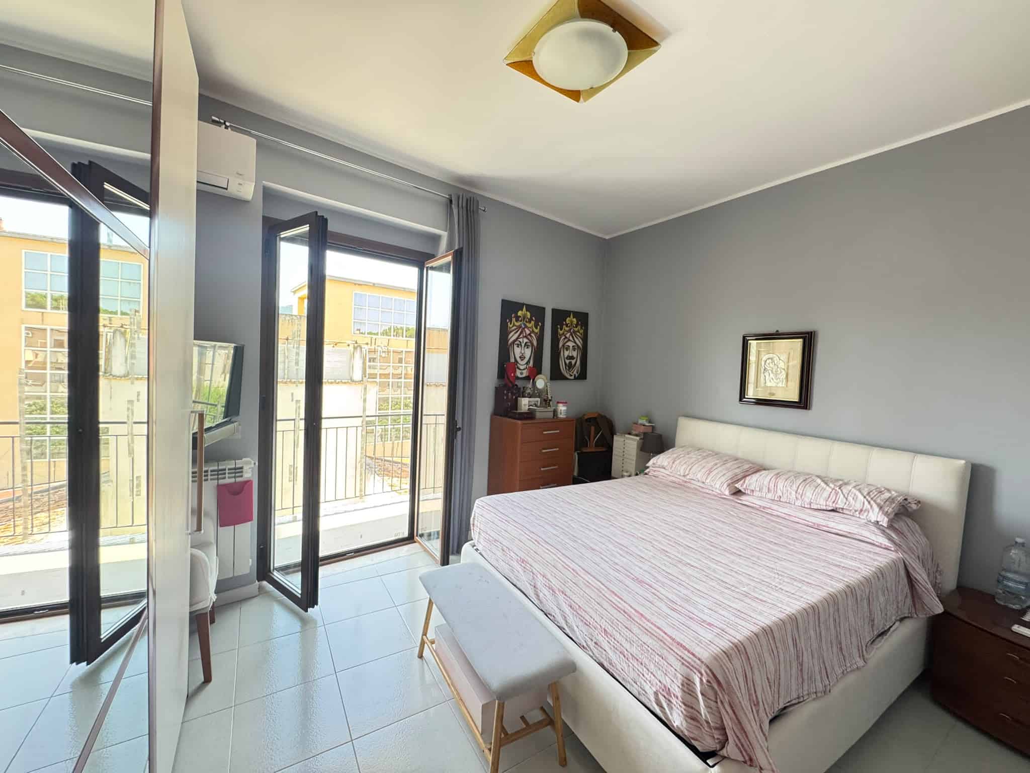 Camera da letto moderna con letto matrimoniale, armadio e balcone con vista sulla città, ambiente luminoso e accogliente.