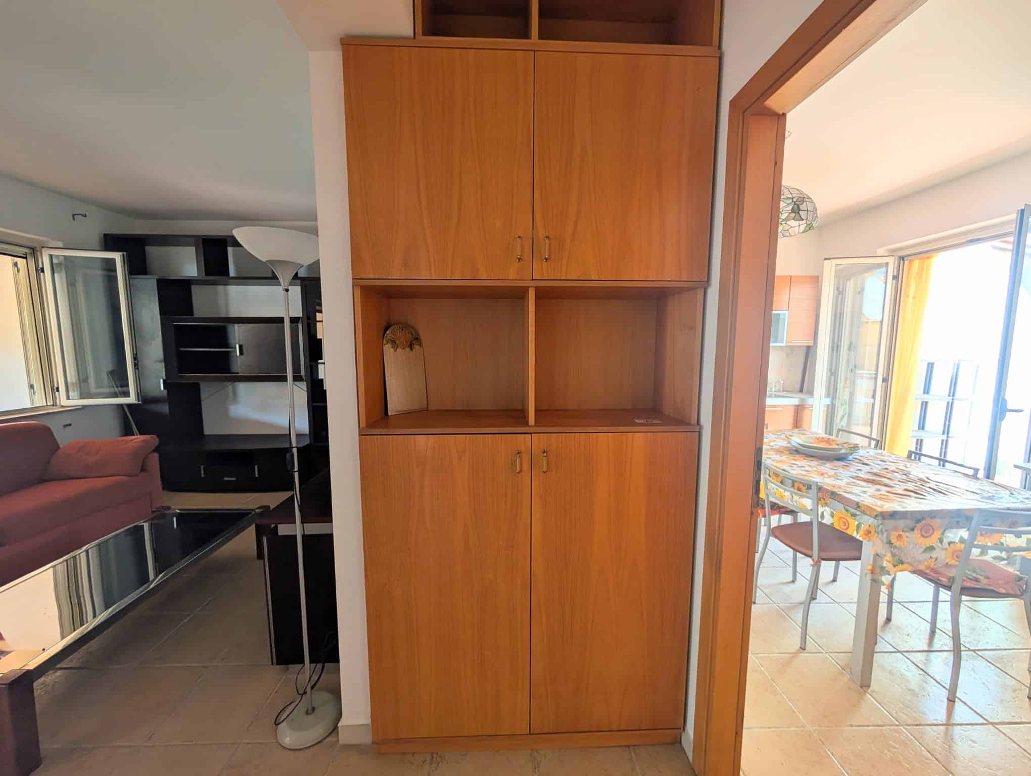 Armadio in legno in una casa con soggiorno e sala da pranzo visibili sullo sfondo.