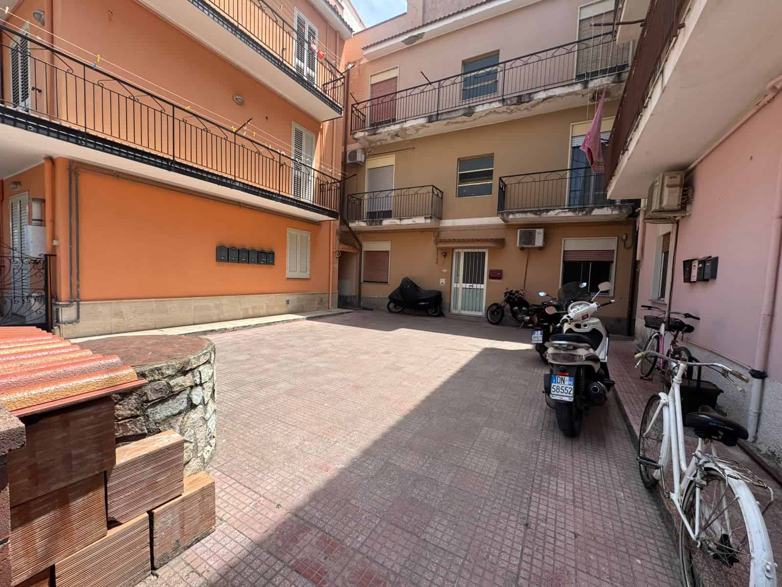 Cortile condominiale di un appartamento in vendita a Oliveri, con biciclette e scooter parcheggiati.