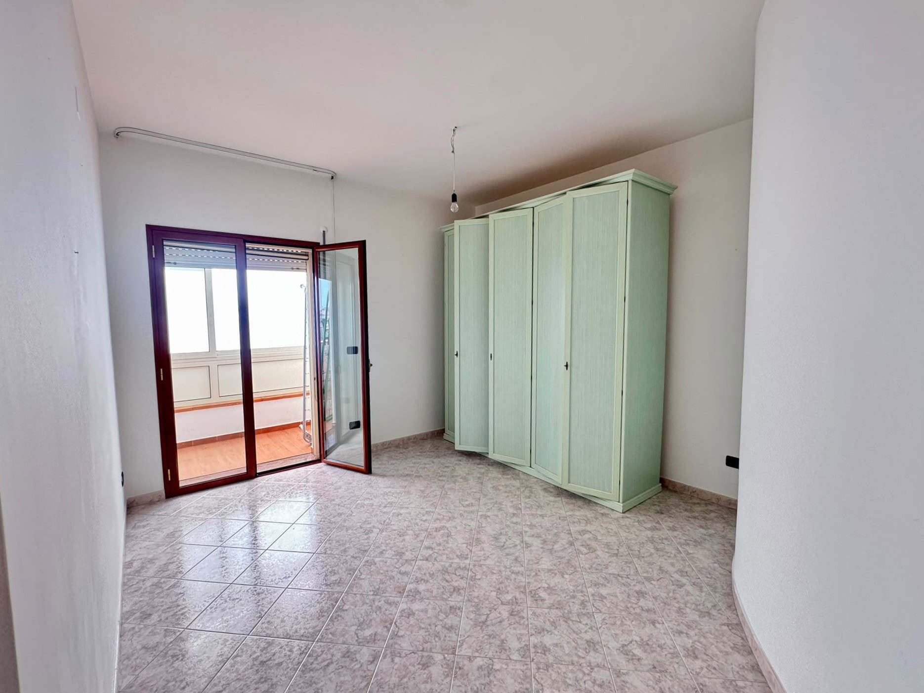 Camera da letto vuota con armadio verde e balcone con porta scorrevole in legno.