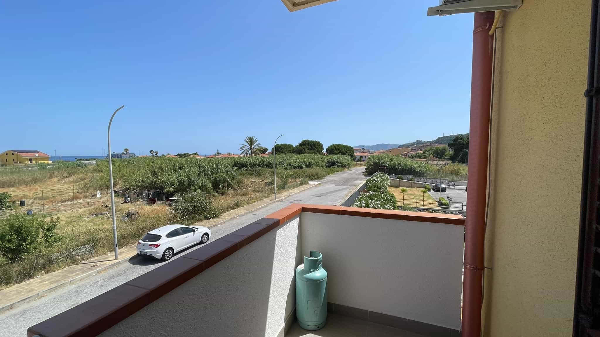 Balcone con vista panoramica sul mare e sulla campagna di Spadafora, con strada e auto in primo piano, cielo sereno e paesaggi naturali sullo sfondo.