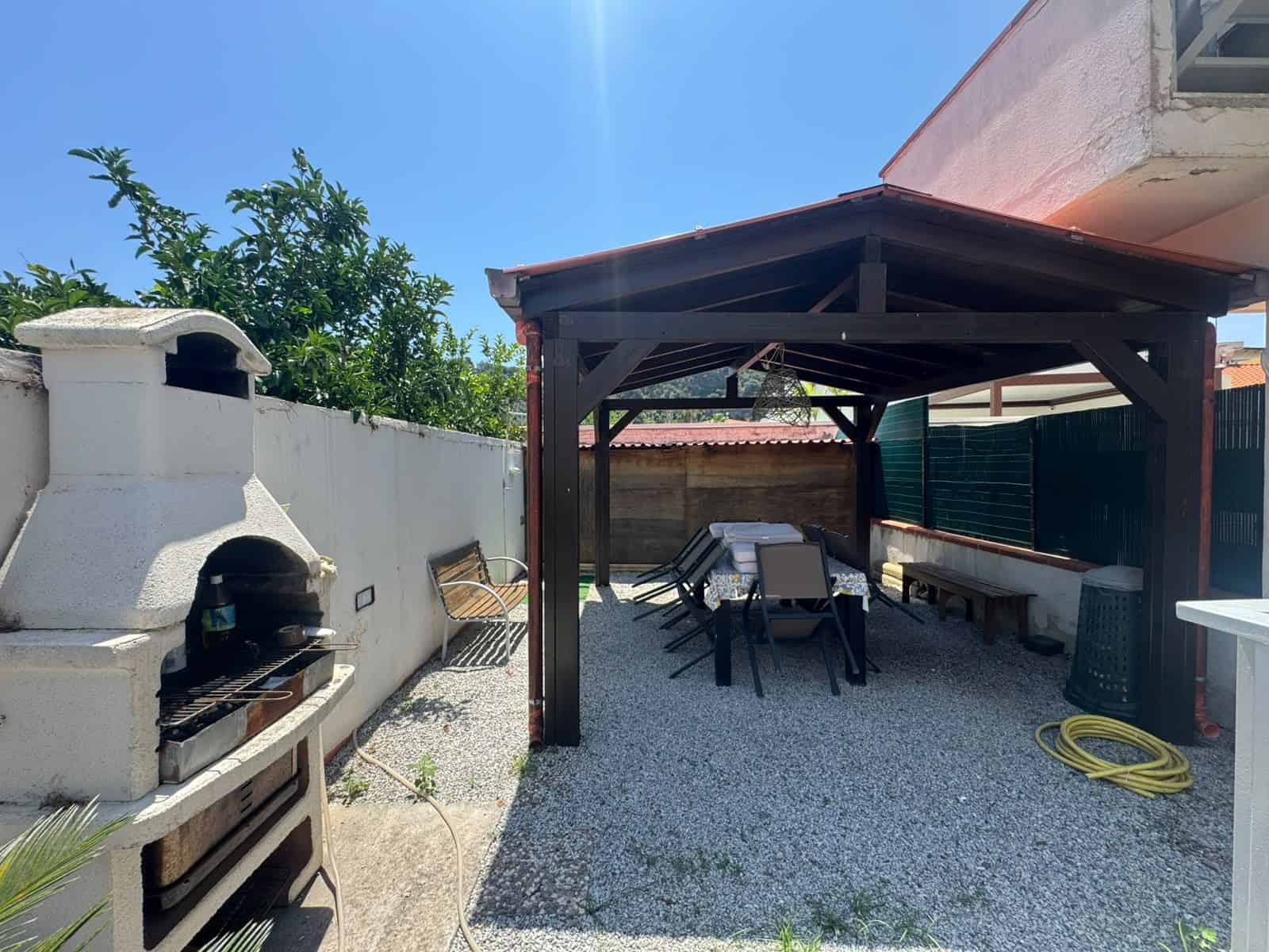 Spazio esterno con barbecue, tavolo e sedie sotto tettoia in una villa a Milazzo.
