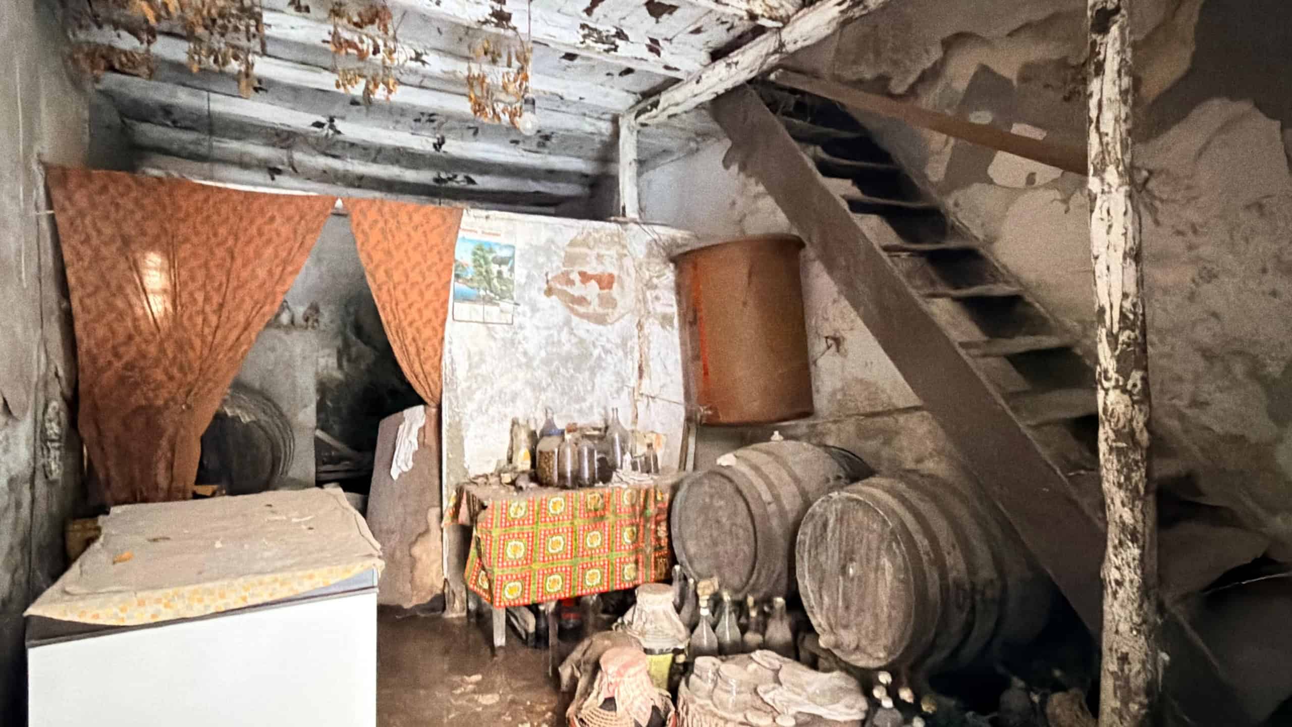 Interno di una cantina rustica con botti di legno e oggetti vari, ambiente antico e trascurato.