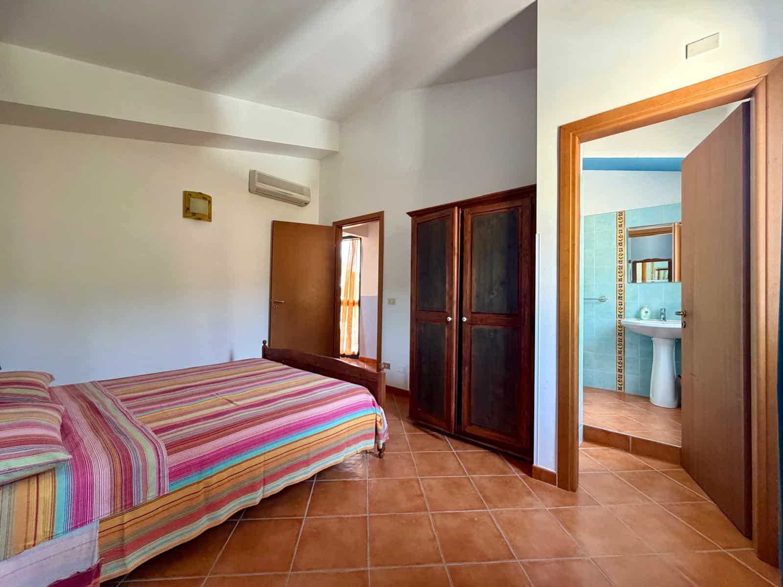 Camera che mostra una camera da letto con letto a due piazze, armadio in legno e accesso al bagno con lavabo e WC.