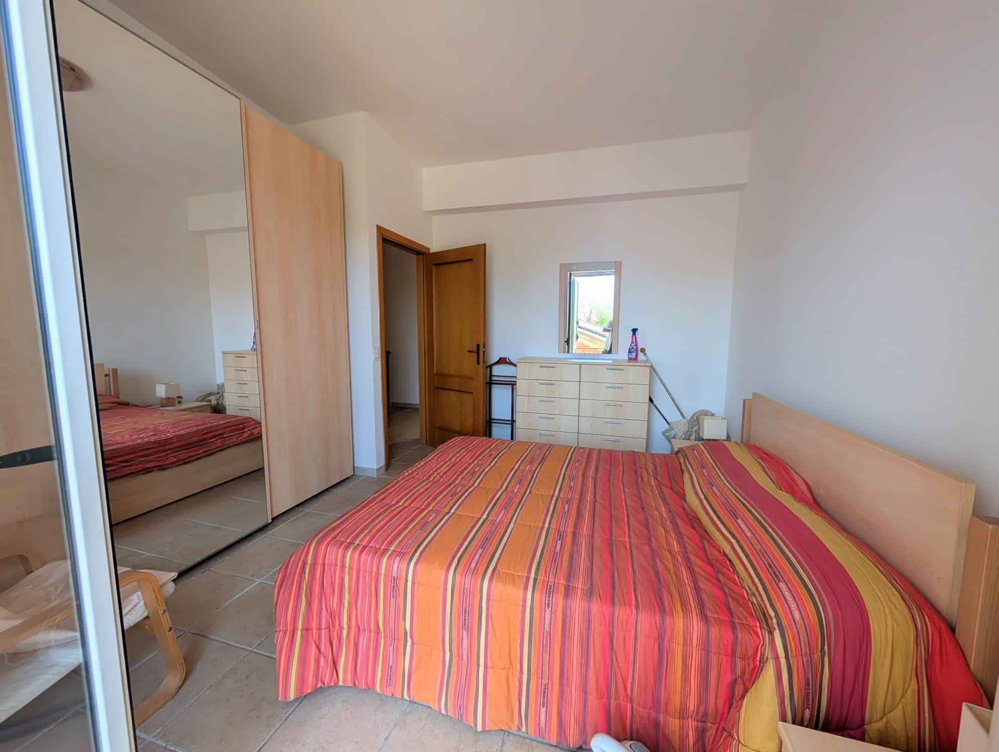Camera che mostra una camera da letto con letto matrimoniale, armadio a specchio e finestra con vista esterna.