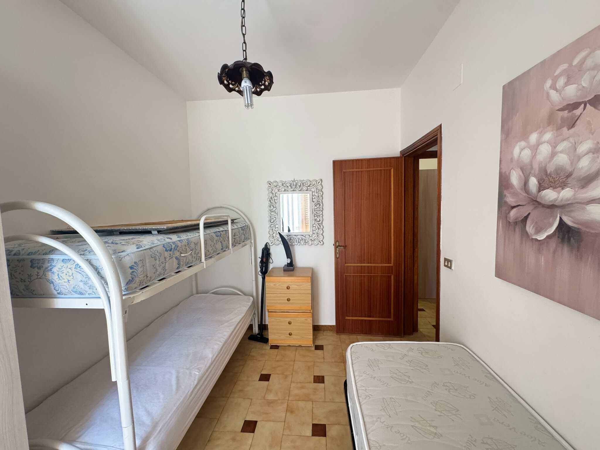Interno di una camera con letto a castello, armadio e decorazioni floreali, in stile semplice e funzionale.