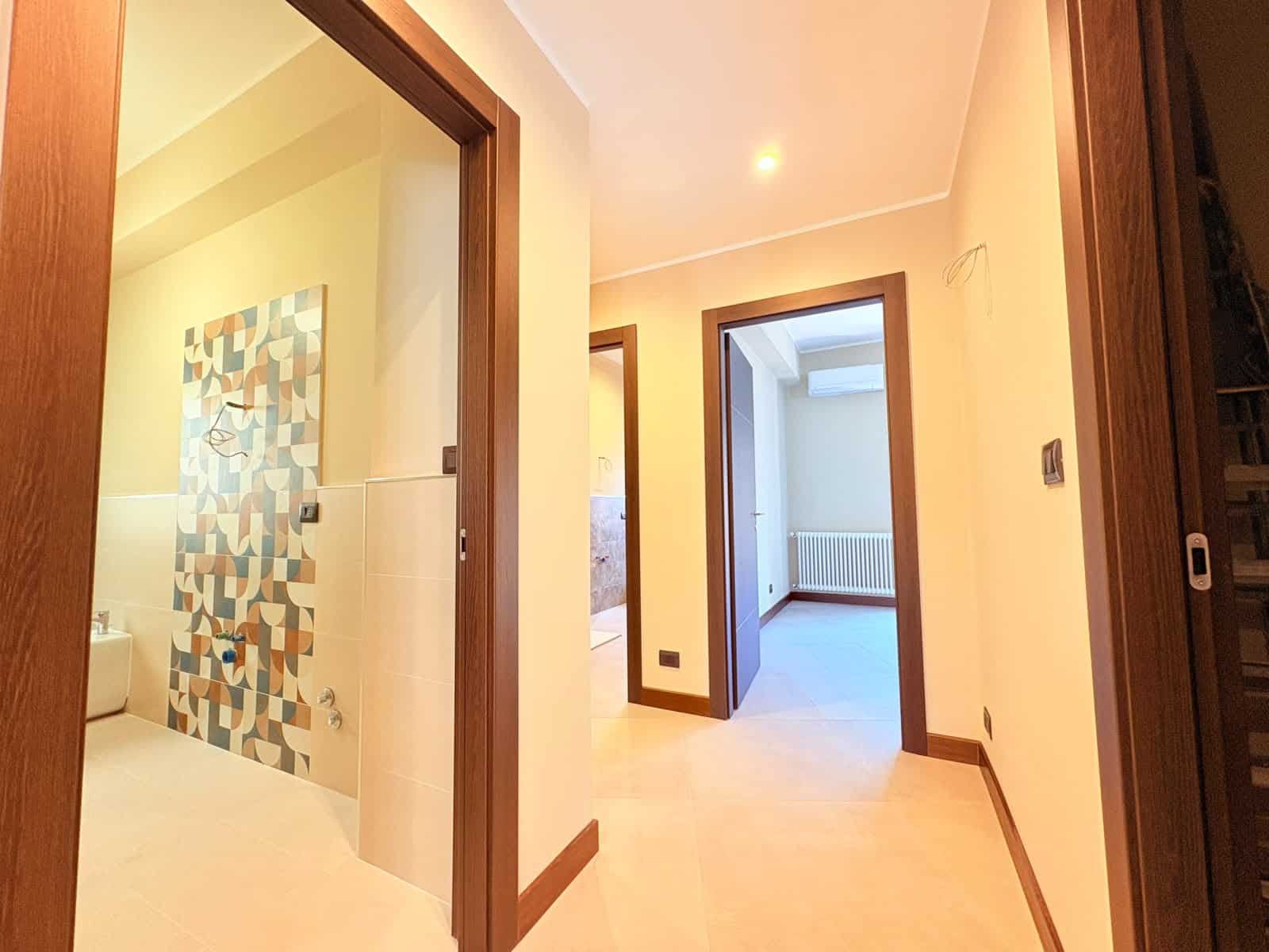Interno di un appartamento in vendita a Milazzo, vista corridoio con porte e pareti bianche, pavimento in legno chiaro.