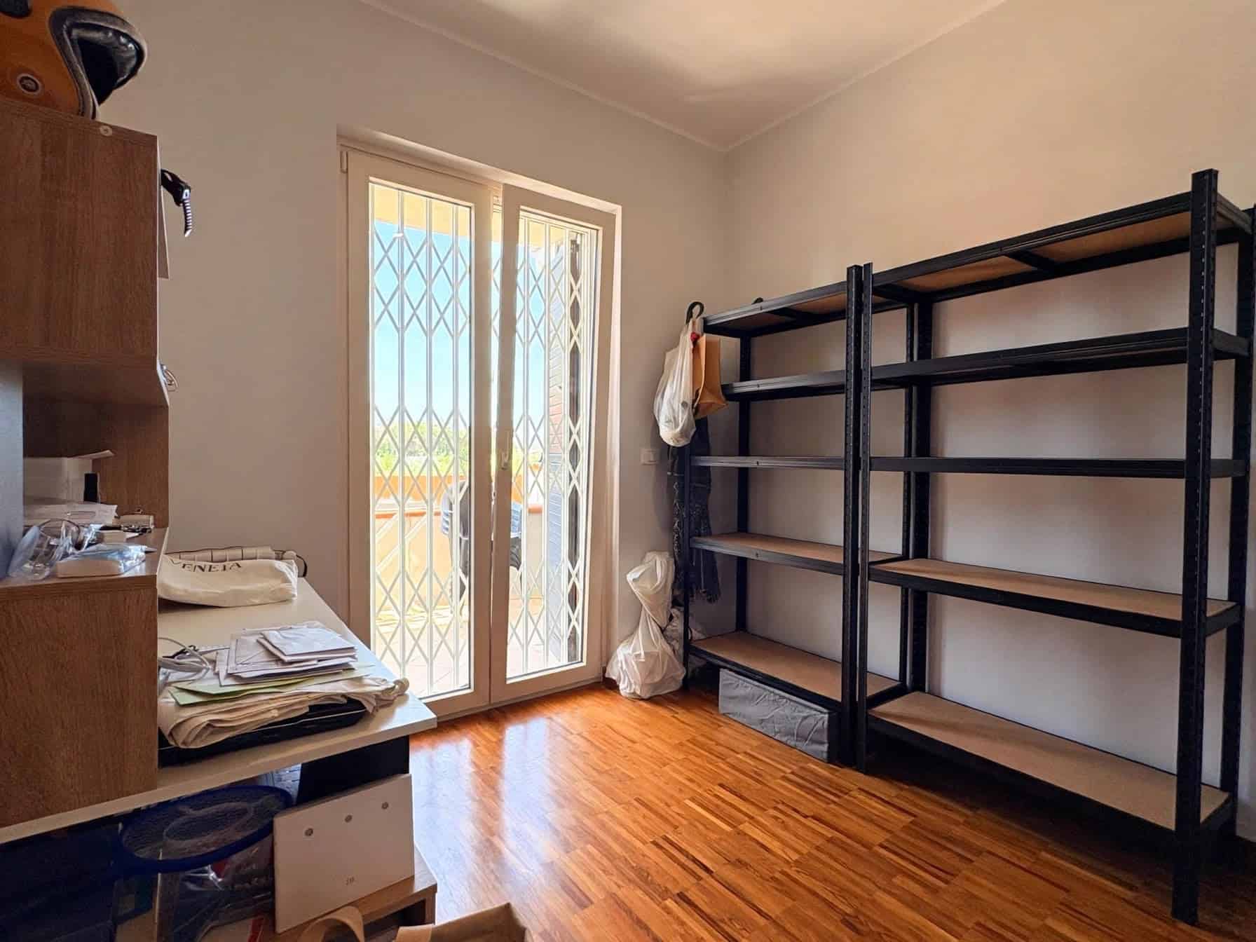 Interno di una stanza in vendita a Milazzo con scaffali neri e porta finestra che dà sul balcone.