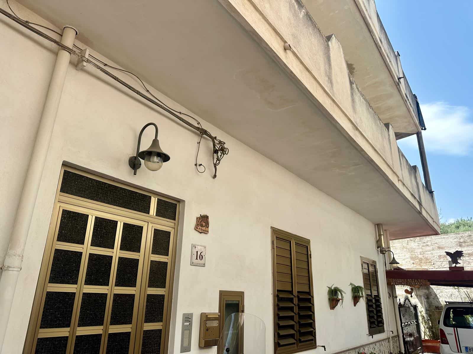 Facciata di un edificio residenziale con balcone e finestre con persiane in alluminio, decorato con piante in vaso.