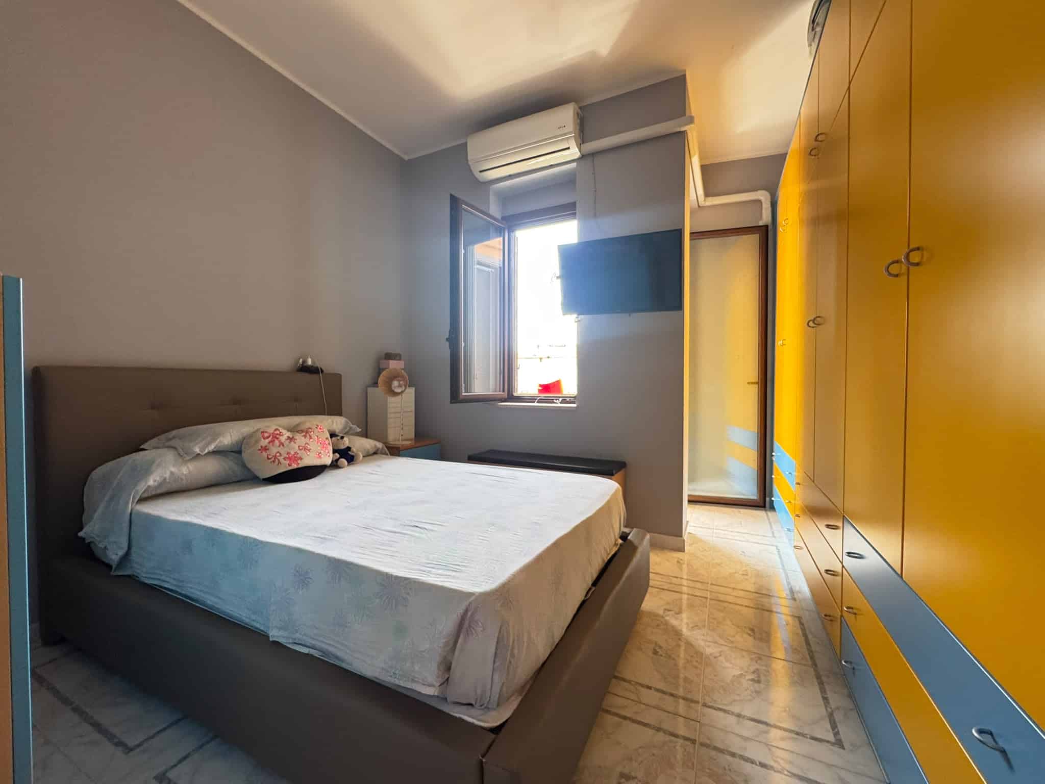 Camera da letto moderna con pareti grigie, armadio giallo e finestra che lascia entrare luce naturale, aria condizionata e decorazioni eleganti.