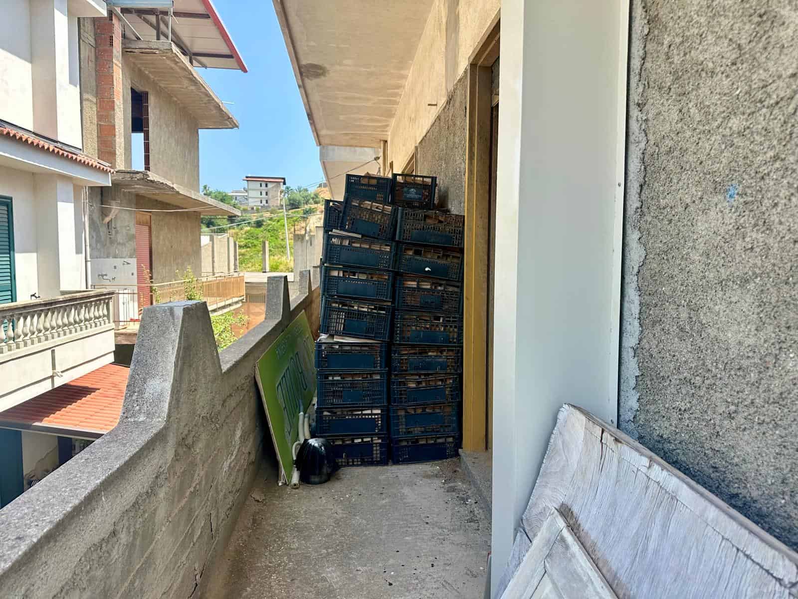 Balcone di un edificio in costruzione con scaffali di plastica pieni di materiali da costruzione e un divano abbandonato.