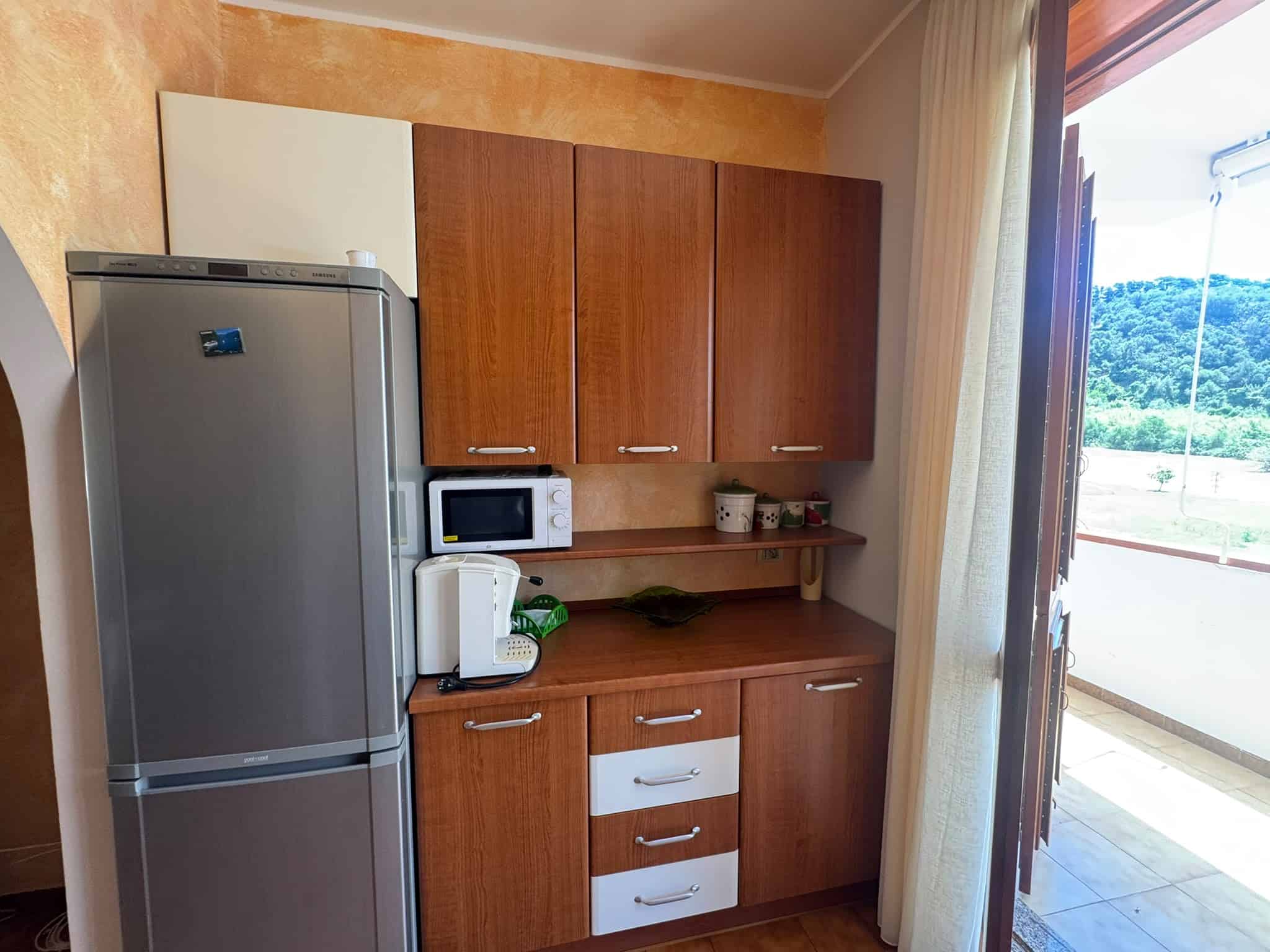 Cucina moderna con frigorifero, microonde e armadietti in legno in un appartamento a Milazzo.