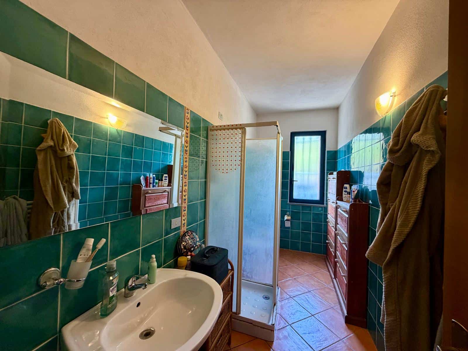 Bagno con pareti rivestite di piastrelle verdi, lavabo, specchio e doccia, ambiente luminoso e funzionale.
