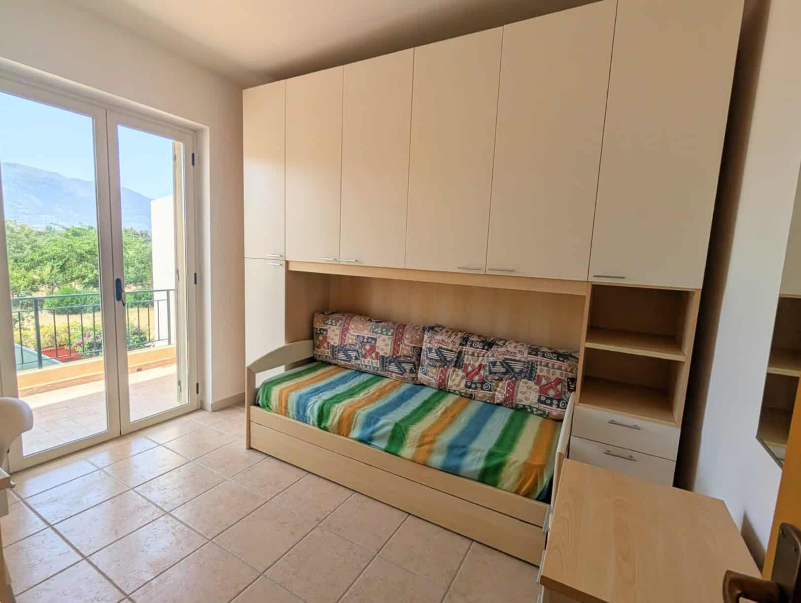 Camera da letto con divano letto, armadi a muro e accesso a un balcone con vista sulle montagne e sulla natura.