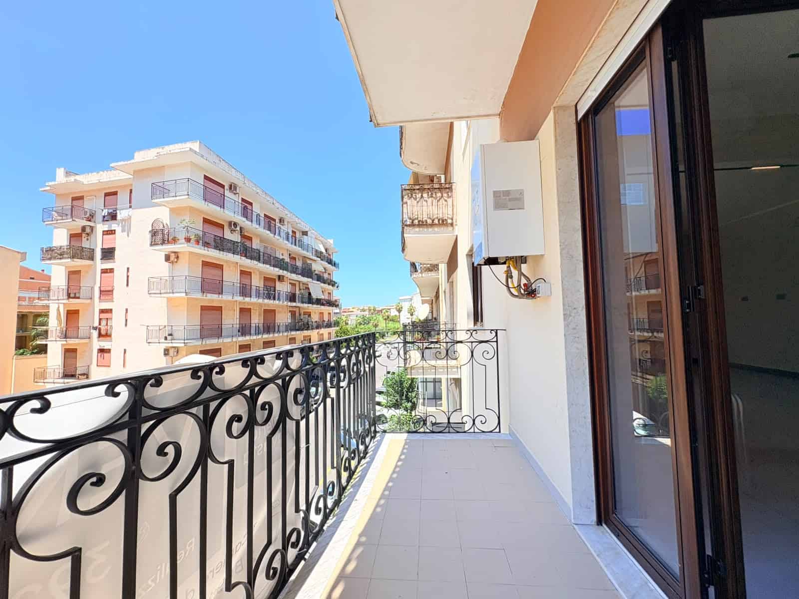 Balcone di un appartamento in vendita a Milazzo con vista su edifici residenziali e cielo azzurro.