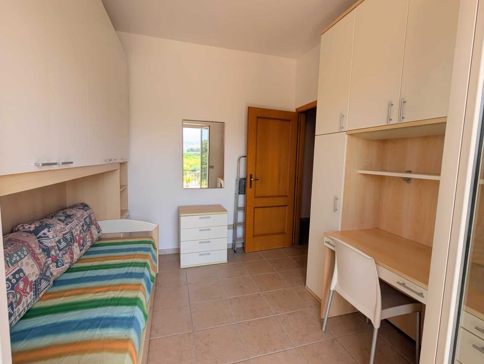 Interno di una villetta a schiera con letto, scrivania e armadi, ambiente luminoso e ben organizzato.