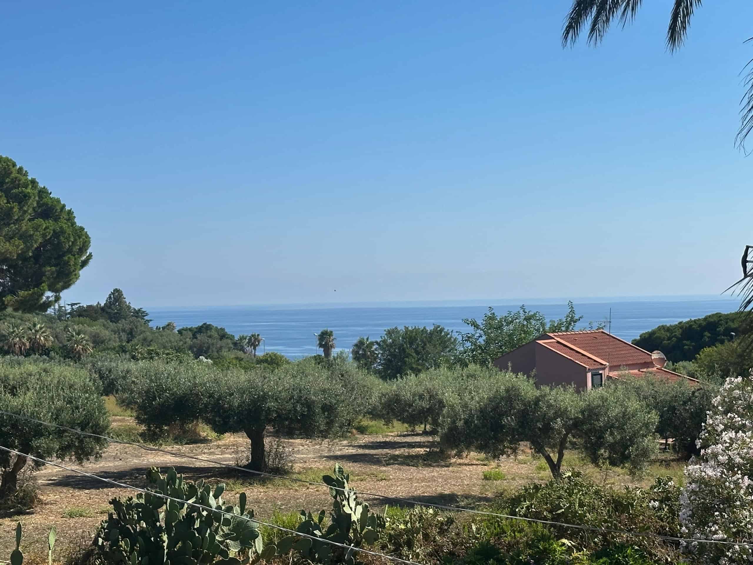 Vista panoramica sulla campagna con vista mare, alberi e un edificio in lontananza a Milazzo, Sicilia.