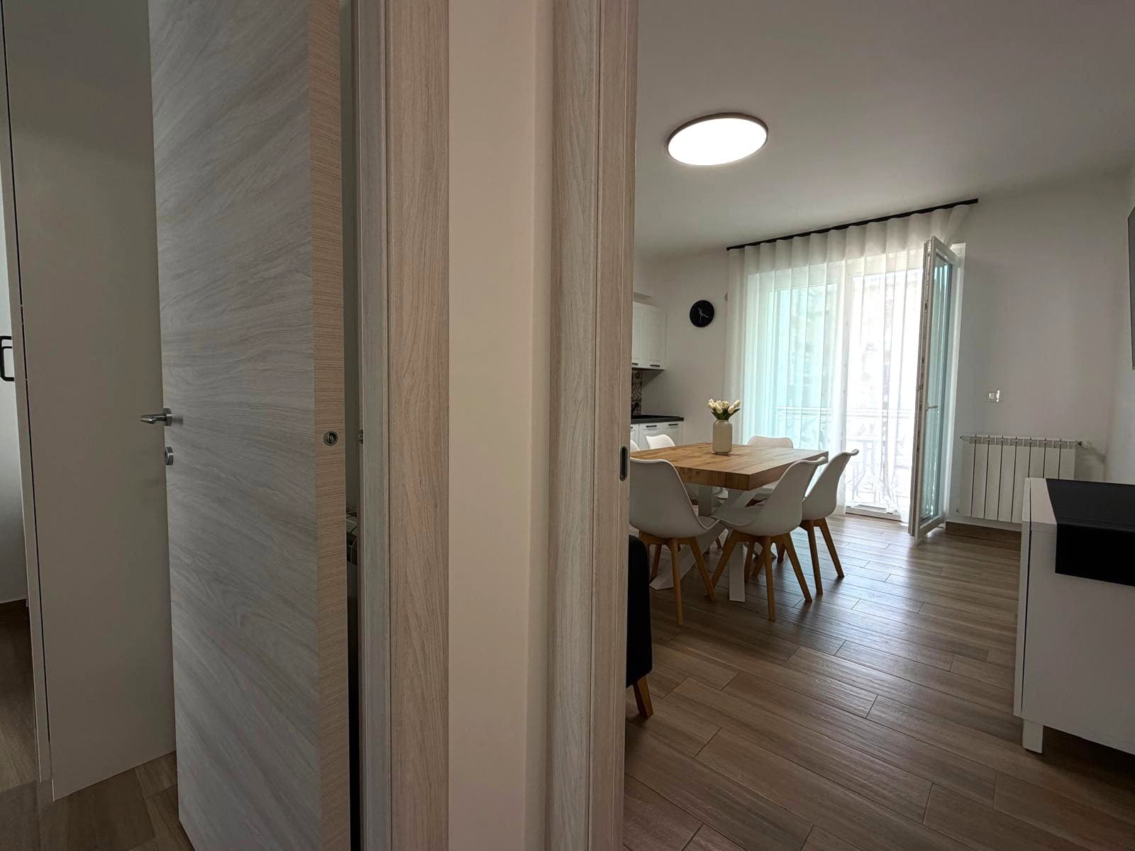 Interno moderno di un appartamento in vendita a Milazzo, con zona pranzo e grande finestra con tende leggere.