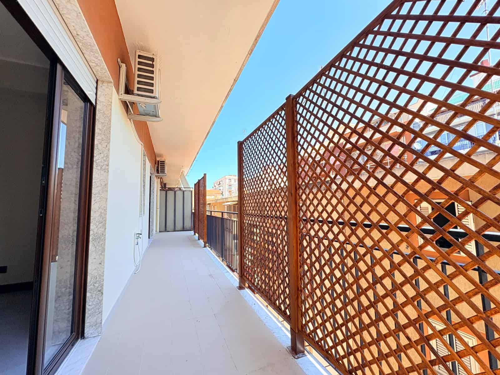 Balcone di un appartamento in vendita a Milazzo con vista sulla città e sul mare, con parapetto in legno e aria condizionata.