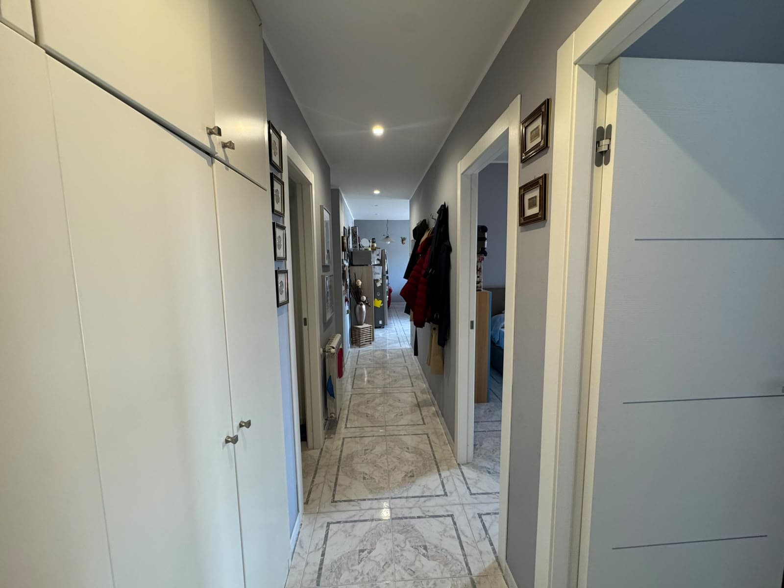 Interno di un appartamento con corridoio, armadi e porte verso le stanze, arredamento moderno e luminoso.