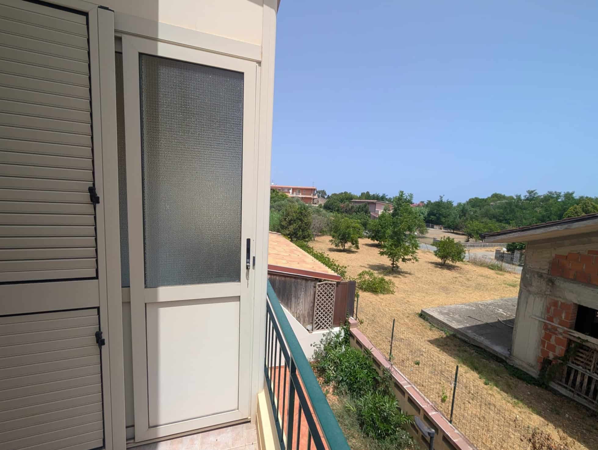 Balcone di una villetta a schiera con vista su un'area verde e case vicine, in un giorno soleggiato.
