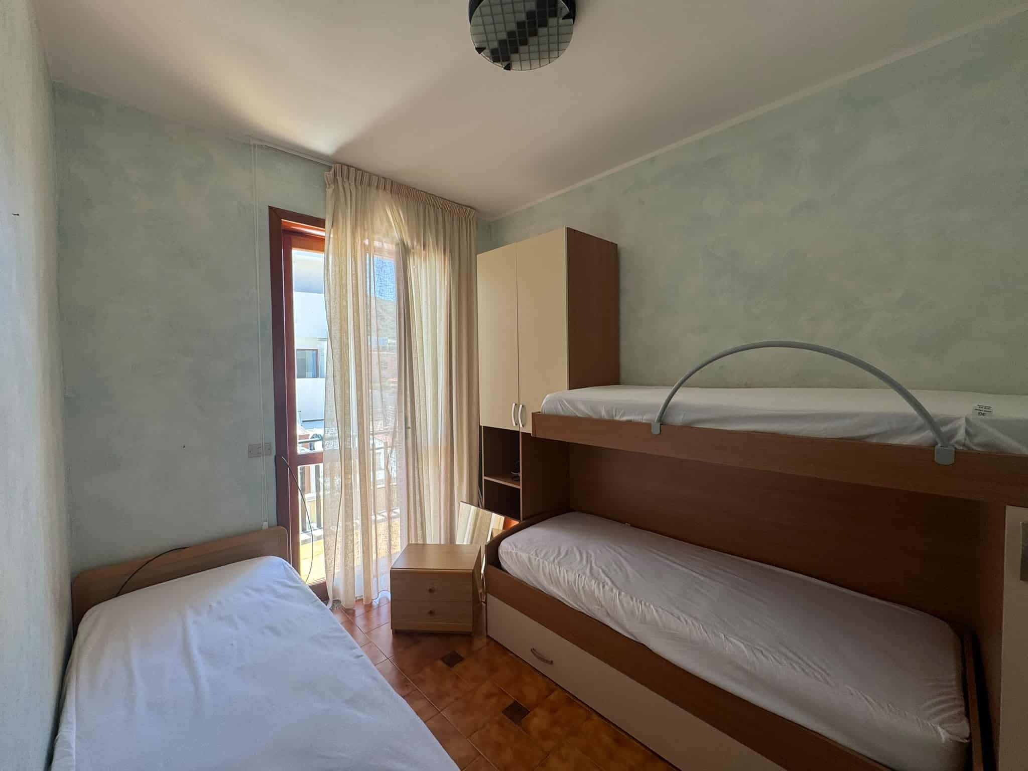 Camera da letto con letti a castello e finestra con tende leggere, in una casa in vendita a Milazzo.