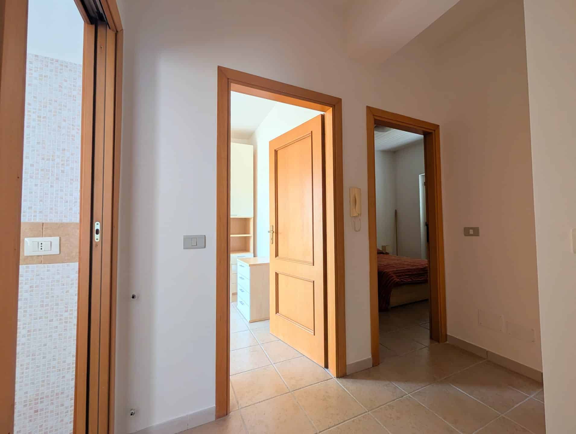Ingresso di una villetta a schiera con porte in legno e pavimento in piastrelle beige.