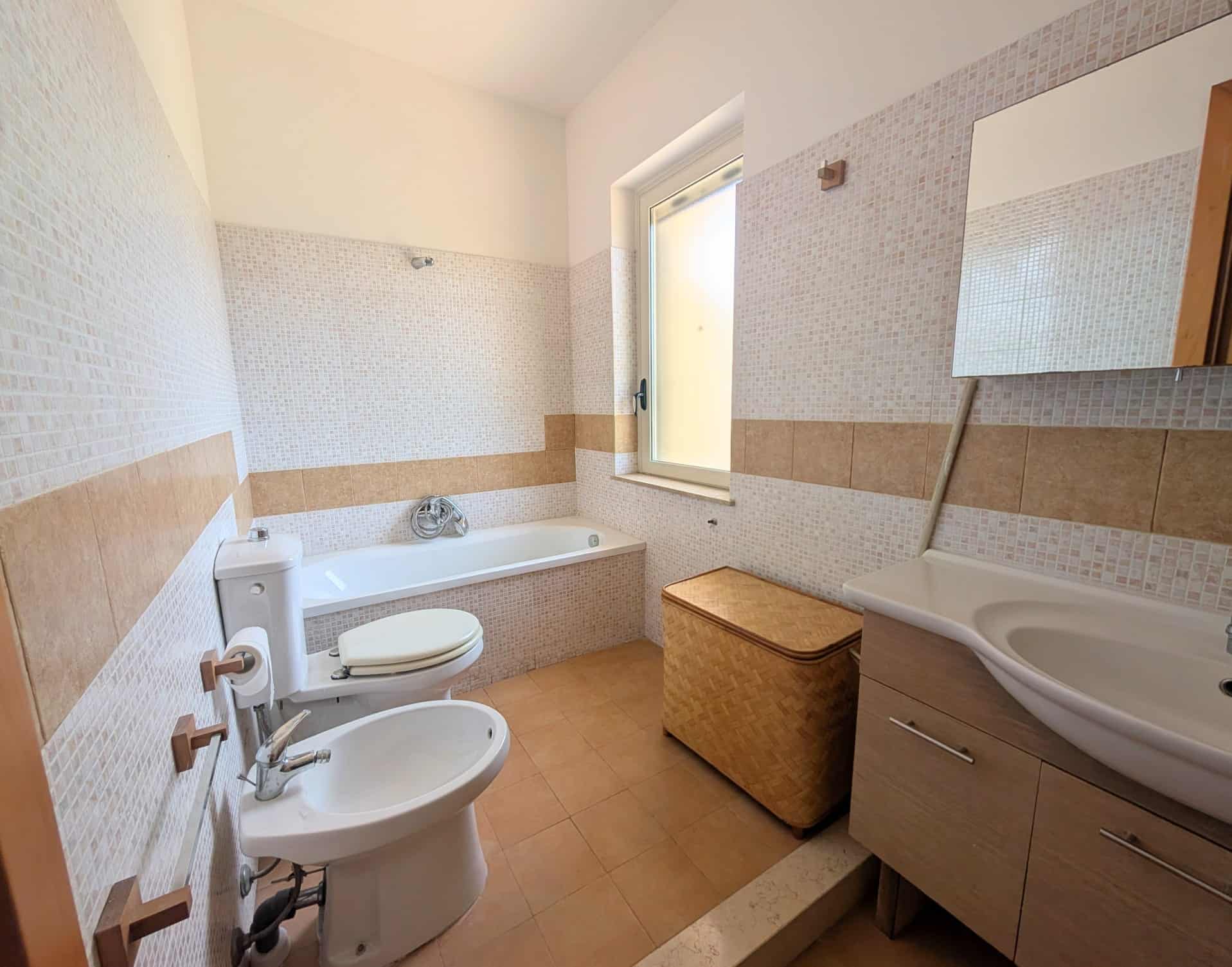 Bagno spazioso con vasca, bidet, lavabo e finestra, arredato in stile semplice e funzionale.