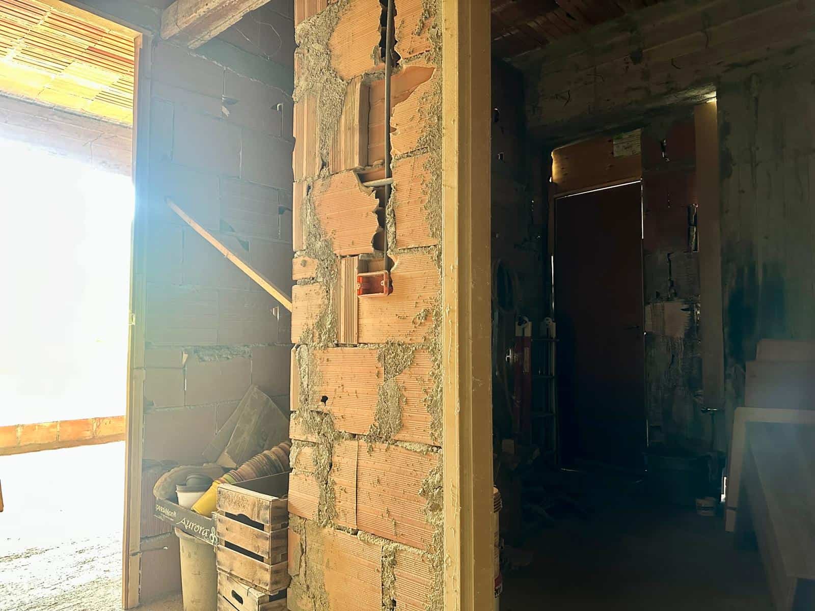 Interno di un edificio in costruzione con pareti in mattoni e struttura in legno, luce naturale che entra da una finestra aperta.
