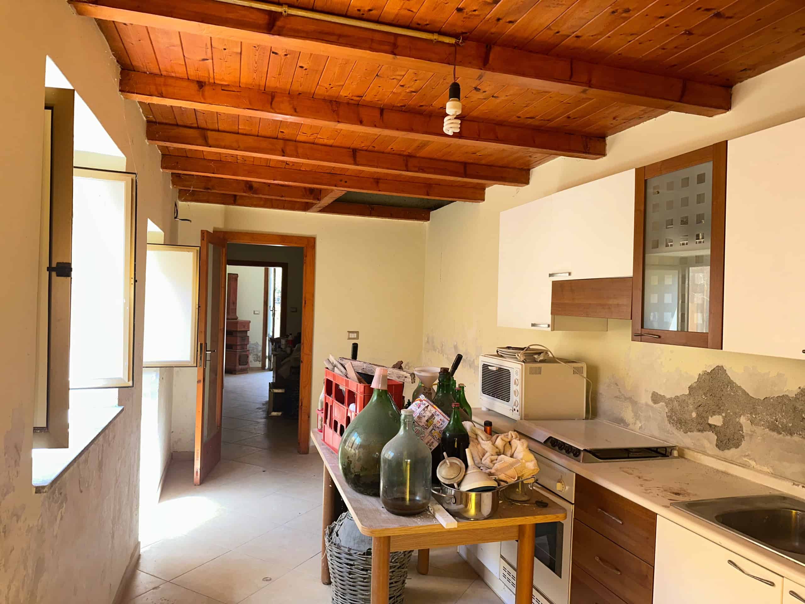 Interno di una cucina rustica con soffitto in legno e pareti bianche, con alcuni oggetti decorativi e elettrodomestici.