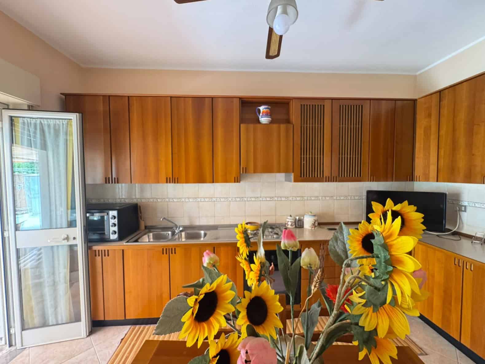 Cucina abitabile con mobili in legno, forno, microonde e frigorifero, decorata con un vaso di girasoli in primo piano.