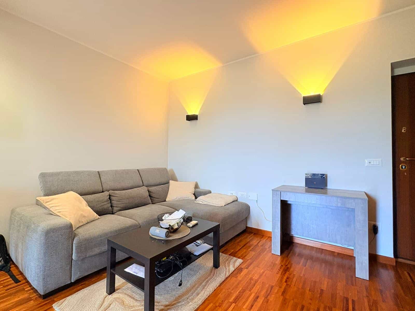 Interno di un soggiorno moderno con divano grigio, tavolino e illuminazione soffusa, in un appartamento in vendita a Milazzo.
