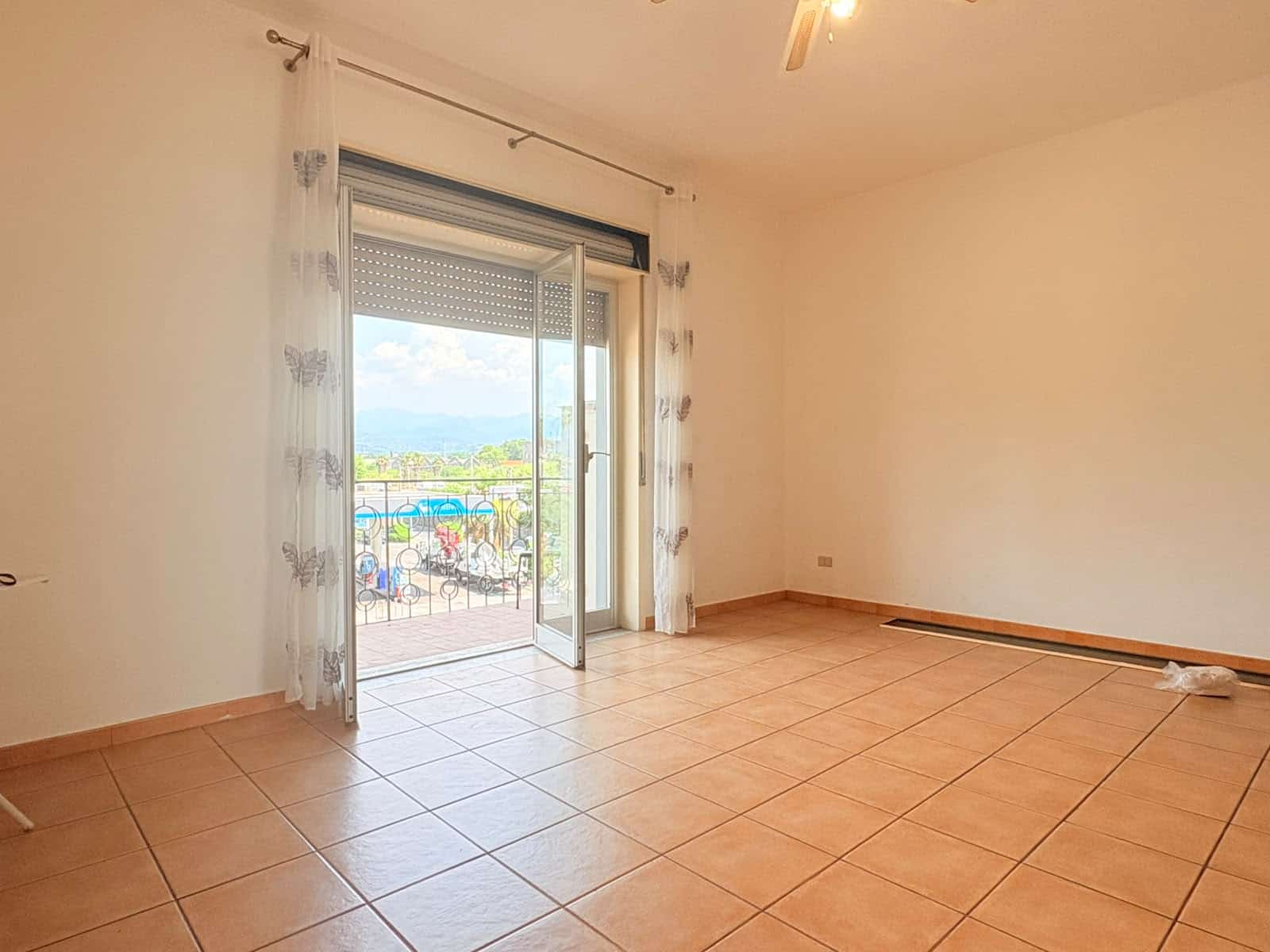 Stanza luminosa con porta finestra che dà su un balcone con vista panoramica.