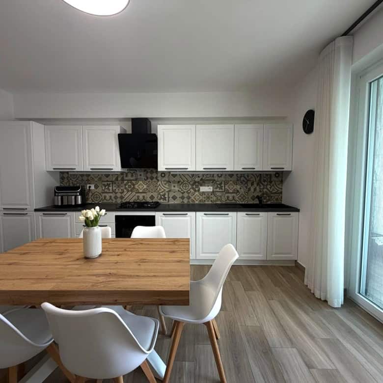Cucina moderna con mobili bianchi, tavolo in legno e sedie bianche, grande finestra con tende trasparenti, ideale per appartamento in vendita a Milazzo.