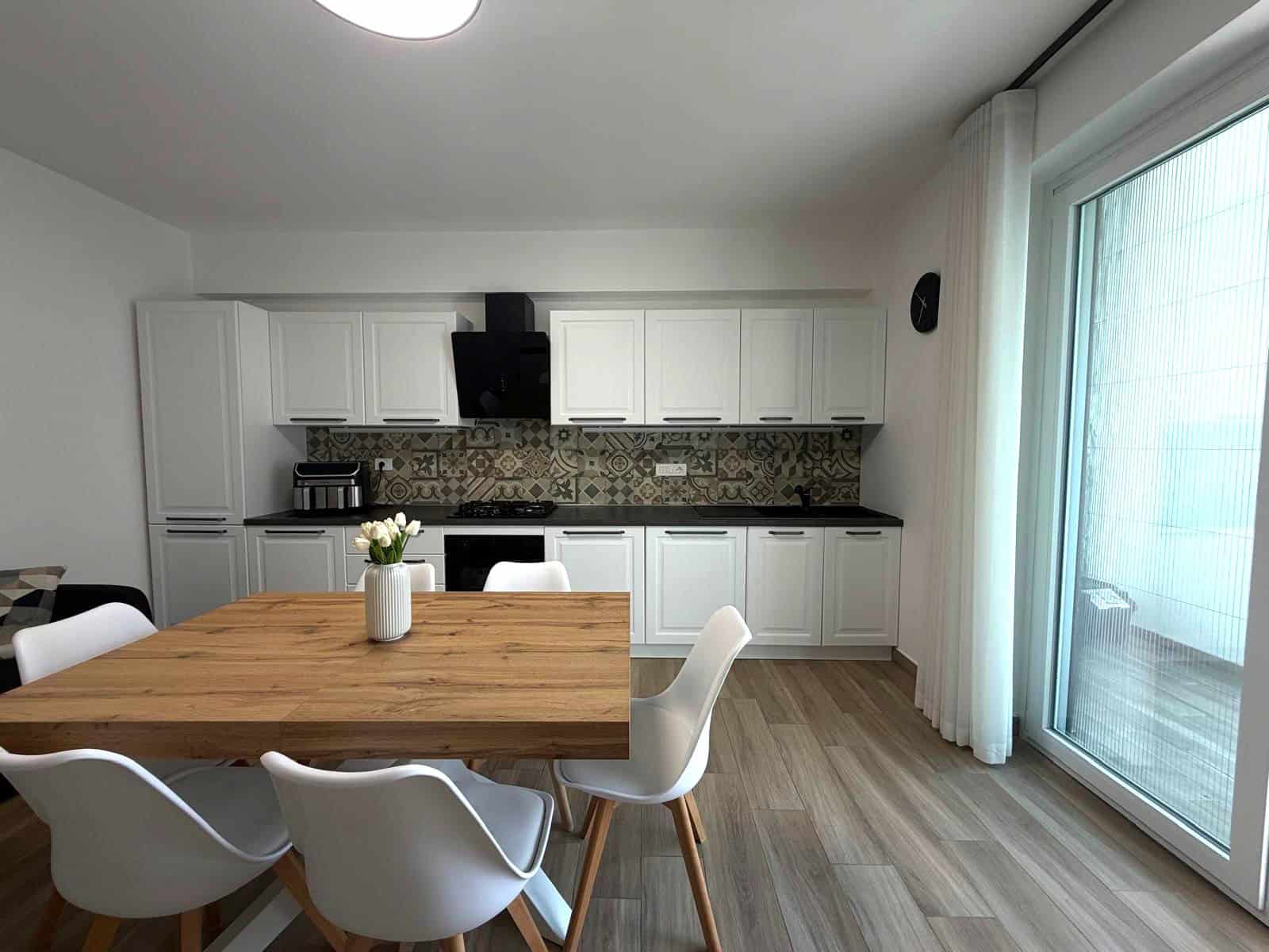 Cucina moderna con mobili bianchi, tavolo in legno e sedie bianche, grande finestra con tende trasparenti, ideale per appartamento in vendita a Milazzo.