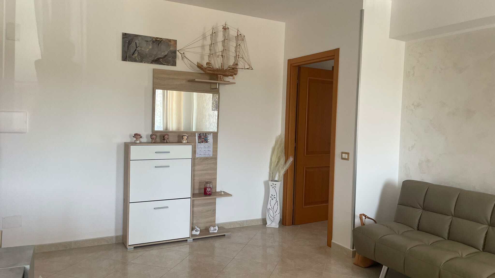 Interno di un soggiorno di un appartamento in vendita a Spadafora, con divano beige e mobile con decorazioni e modellino di nave in legno.