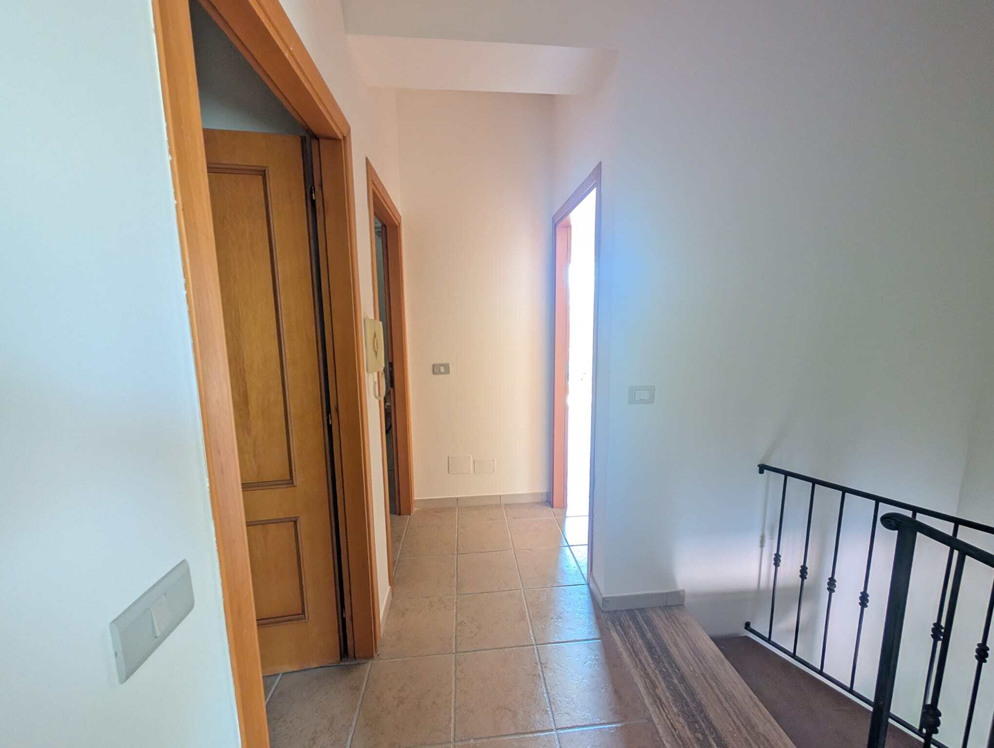 Ingresso luminoso di una villetta a schiera con pareti bianche, porte in legno e un corridoio ben illuminato.