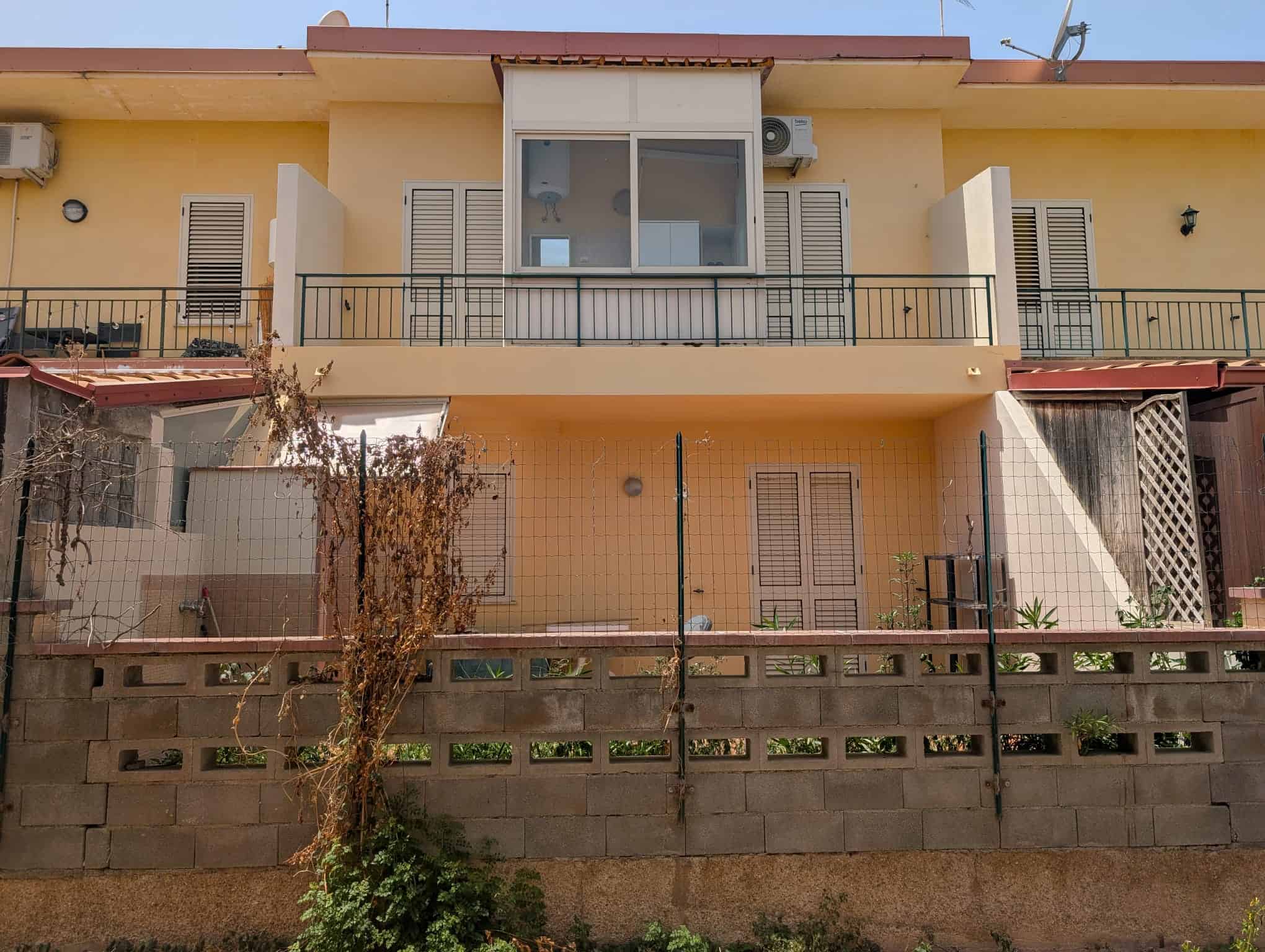 Villetta a schiera con balcone, giardino e facciata gialla, ideale per famiglie, in zona residenziale.