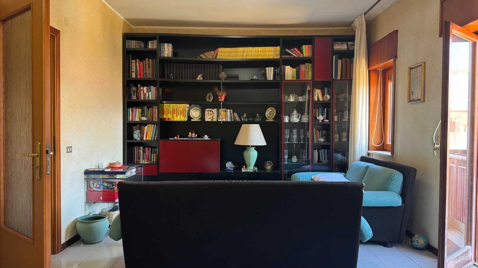 Interno di un soggiorno con libreria a parete, divano blu e finestra con vista sulla città di Messina.