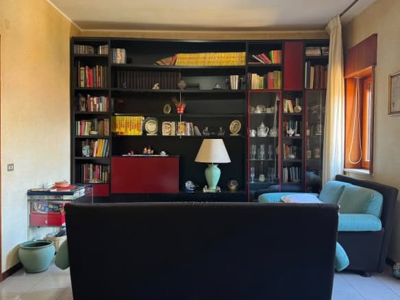 Salotto in stile classico con libreria a parete, divano blu e finestra luminosa, ideale per appartamento in vendita a Messina.