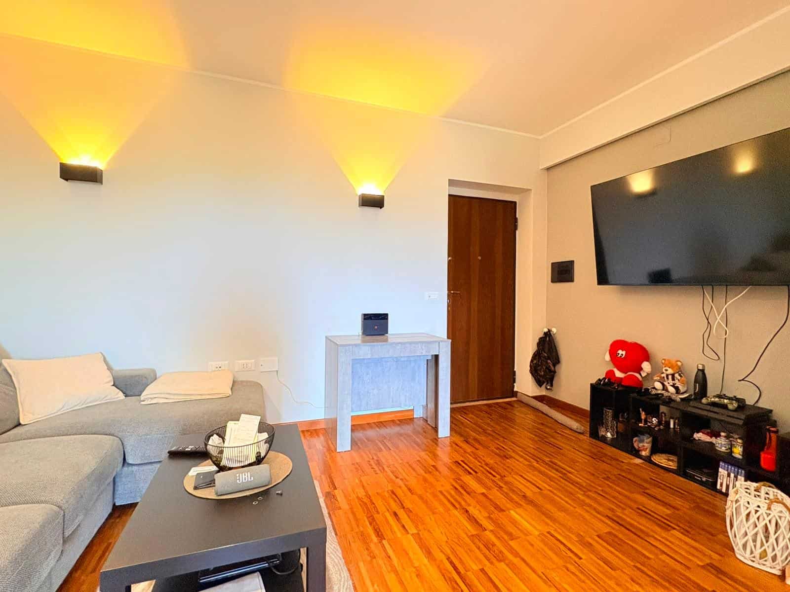 Salotto luminoso con divano grigio, TV grande e pavimento in legno, arredamento elegante e accogliente in appartamento in vendita a Milazzo.