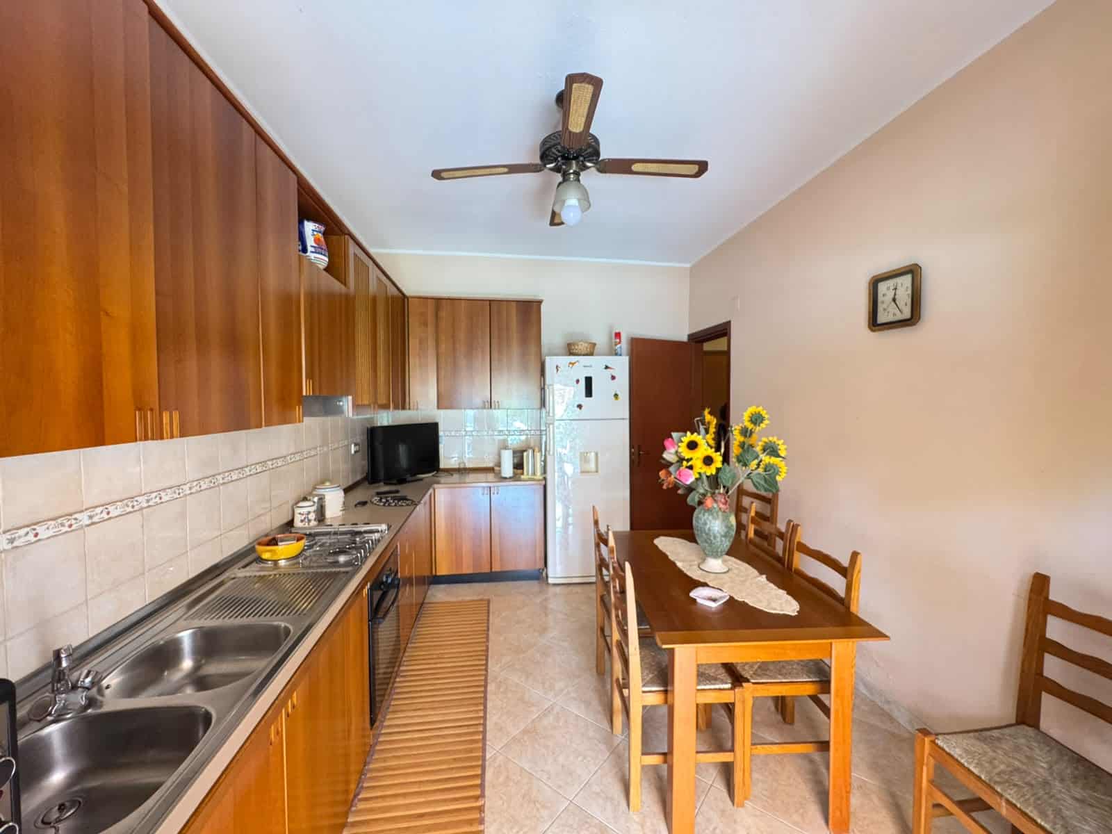 Cucina spaziosa con mobili in legno, tavolo da pranzo e frigorifero in un appartamento in vendita a Oliveri, Me.